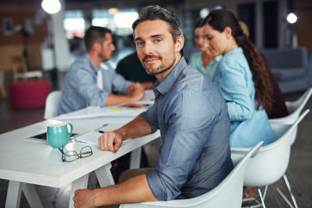 The creative process. Portrait of a mature man sitting at a table in an office with colleagues...