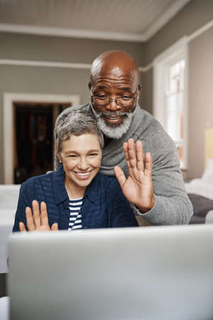 Connect to loved ones wherever you are. Shot of a senior couple waving while using a laptop at home.