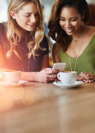 Were besties, of course we have no secrets. Cropped shot of girlfriends sharing something on a cellphone while sitting in a cafe.の写真素材