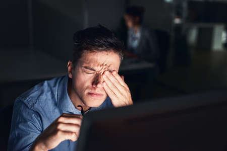 How can I be productive with this headache. Shot of a young businessman working late at night in a modern office.の写真素材