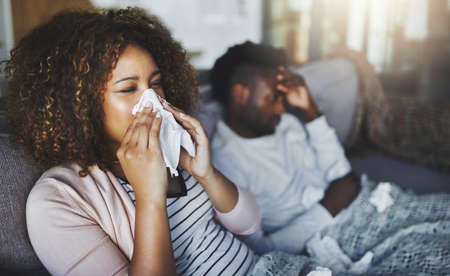 Time to stock up on some vitamin C. Shot of a young woman blowing her nose with her boyfriend in the...