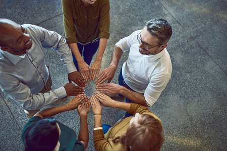 Getting the job done as one. High angle shot of a group of colleagues joining their hands in solidarity at work.の写真素材