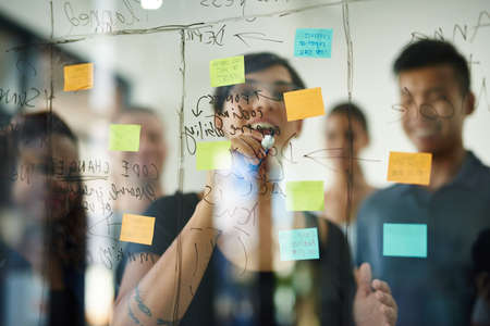 Planning is the first step. Cropped shot of a group of young designers planning on a glass board.