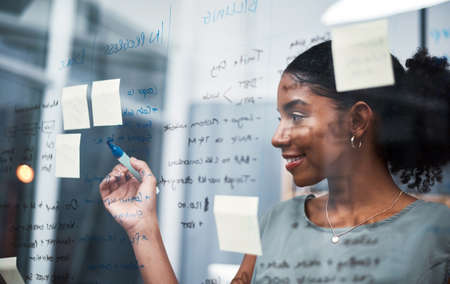 The expert mind behind an expert plan. Shot of a young businesswoman brainstorming with sticky notes...