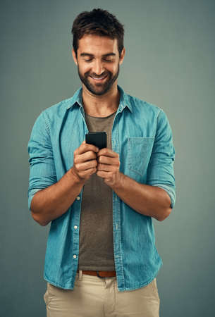 Hes the one everyone wants to be in contact with. Studio shot of a handsome young man using a...