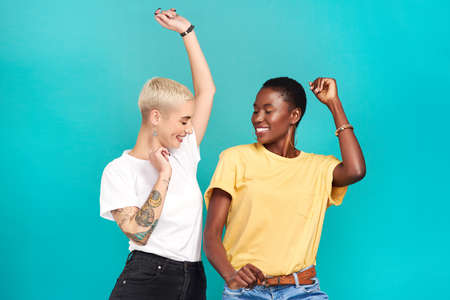 Grab your girl and get grooving. Studio shot of two young women dancing together against a turquoise background.の写真素材