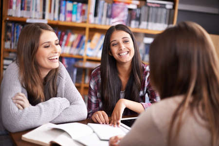 Laughter helps you learn. Cropped shot of three female university students working in the campus library.の写真素材