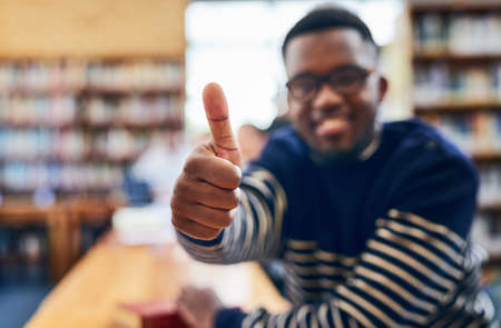 Im positive about my future. Shot of a student showing thumbs up while sitting in the library.の写真素材