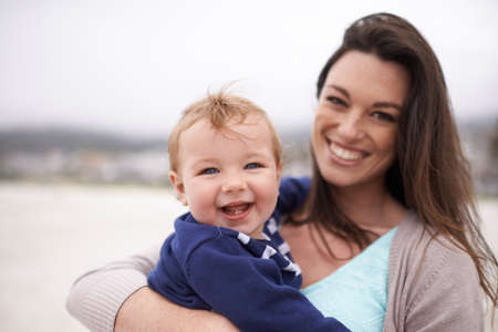 Mommy and me time at the beach. Portrait of a an attractive young woman holding her baby boy at the beach.の写真素材