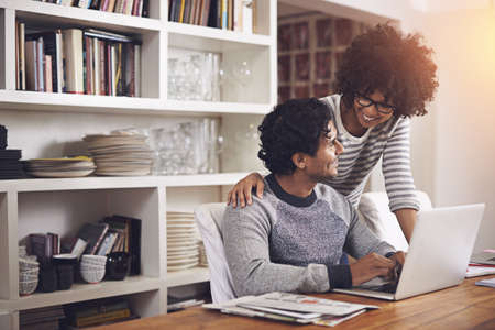 Can I get you a sandwich, honey. Shot of a young woman standing by her husband whos using a laptop.の写真素材