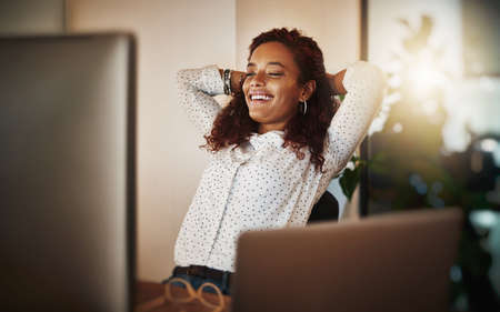 At the end of the day it was worth it. Shot of a young businesswoman taking a break at her desk in a modern office.の写真素材