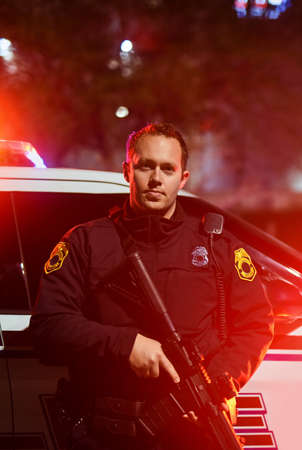 Some situations require more force than others. Cropped portrait of a handsome young policeman standing with his assault rifle while out on patrol.の写真素材