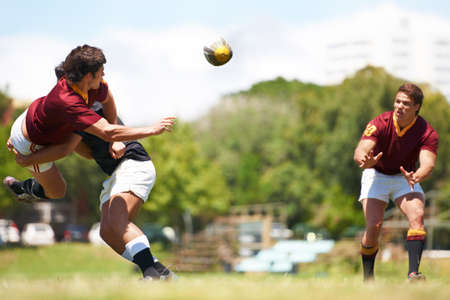 Working together for stronger unity. Shot of a young rugby player executing a pass mid-tackle.の写真素材