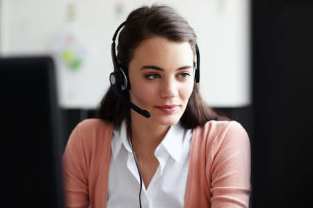 Conscientious young worker. A pretty young woman wearing a headset looking at her computer screen.