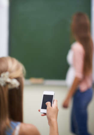 Looking for answers on her mobile. Over the shoulder shot of a young girl using her cellphone in class.の写真素材