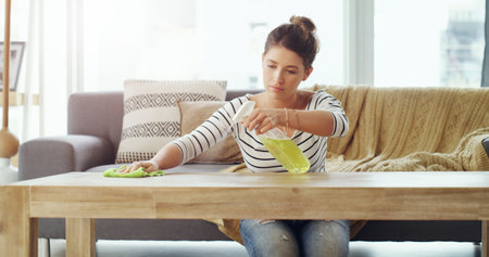 I want this place to be spotless. Shot of a young woman cleaning the table in her living room.