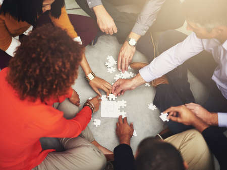 Piece by piece. High angle shot of a group of coworkers putting a puzzle together.の写真素材