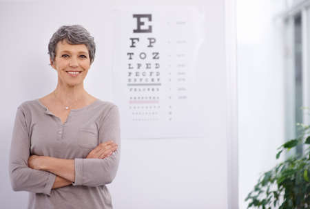 Eye health is fundamental. Portrait of a female optometrist standing beside an eye test poster.の写真素材