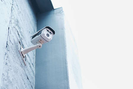 We see trouble coming from a mile away. Low angle shot of a security camera mounted on a wall outside a building.の写真素材