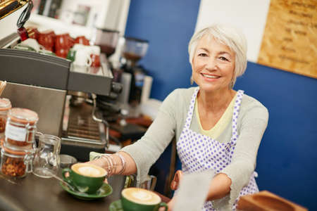 Forget the rest, our coffees the best. Shot of a senior woman serving coffee in a cafe.の写真素材