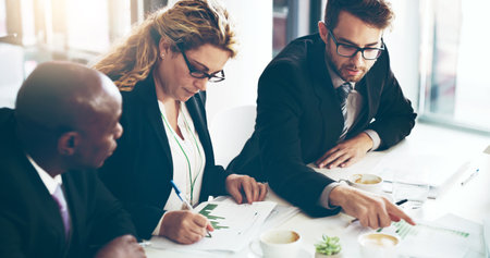 Theyll come up with a strategy. High angle shot of a group of corporate businesspeople looking at paperwork in the boardroom.の写真素材
