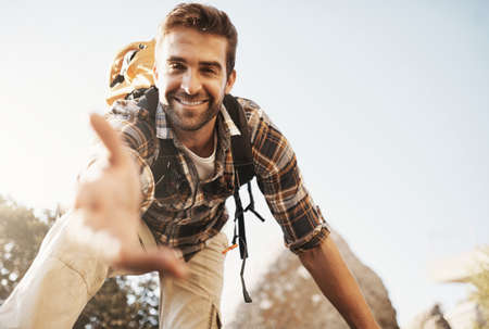 Lemme give you a hand up. Cropped portrait of a handsome young man offering you a hand while hiking in the mountains.の写真素材