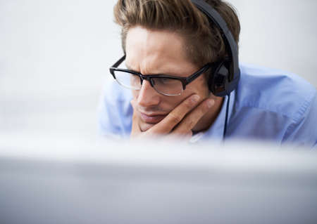 Absorbed in his work. A handsome young businessman wearing a headset while concentrating on his computer screen.の写真素材