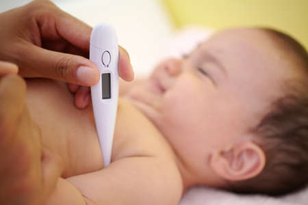 Avoiding a fever. A cute baby girl laughing as her mother is taking her temperature under her arm.
