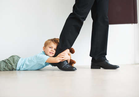 Separation anxiety in action. Portrait of a cute young boy holding onto his dads leg as he tries to leave for work.の写真素材