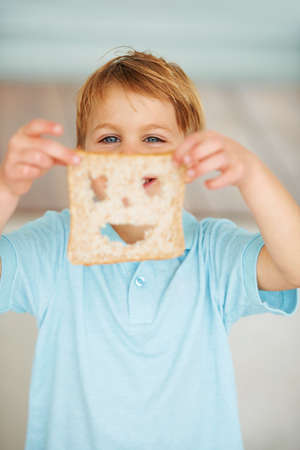 Food makes me happy. Shot of a little boy holding up a slice of bread with a cut out smiley face.