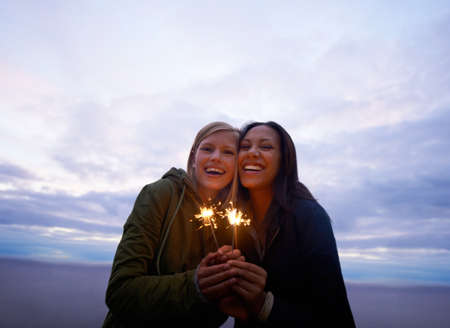 Celebrating the start of an awesome holiday. Two young women holding sparklers with the ocean and...