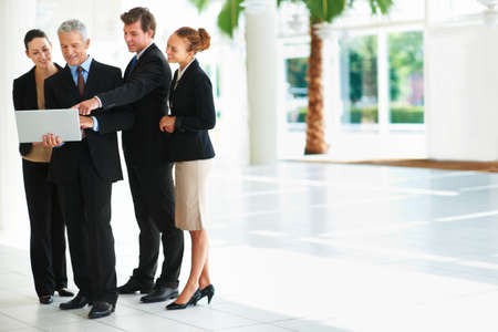 Making business happen. Shot of a group of businesspeople talking over a laptop while standing in an office lobby.の写真素材