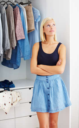 Picturing the perfect outfit. Young woman standing with her arms folded in front of a wardrobe and looking contemplative.の写真素材