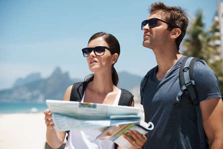 I think its time to ask for directions. Shot of a young couple looking at a map while standing on a...