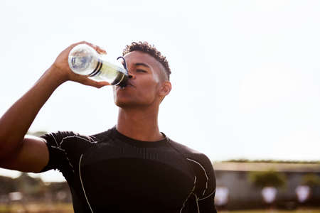 Get hydrated, were going in for the second half. Shot of a young man drinking water after playing a game of rugby.の写真素材