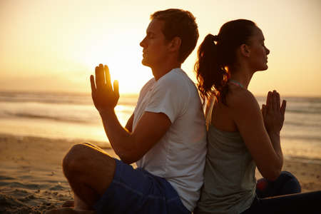 Sunset meditations.... Shot of a couple meditating on the beach at sunset.の写真素材