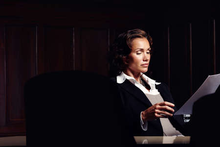 Preparing legal documents. Attractive mature legal woman reading documents at a desk.