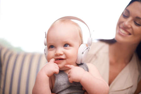 What you listening to. Shot of an adorable baby girl wearing headphones while sitting with her mother.の写真素材