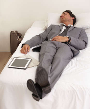 Work exhaustion. A handsome young businessman sleeping on the bed with his digital tablet.の写真素材