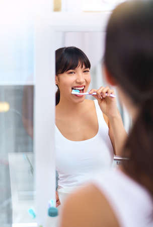 Keeping those pearls white. Shot of a cheerful attractive young woman brushing her teeth while...
