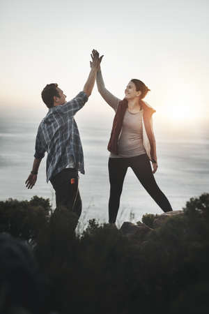 This couple conquered the mountain. Shot of a young couple high fiving after making it to the top of...