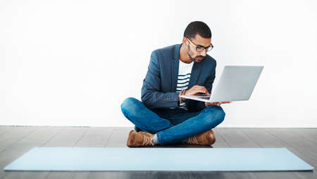 It began with a plan. Studio shot of a young man sitting on the floor and using a laptop while...