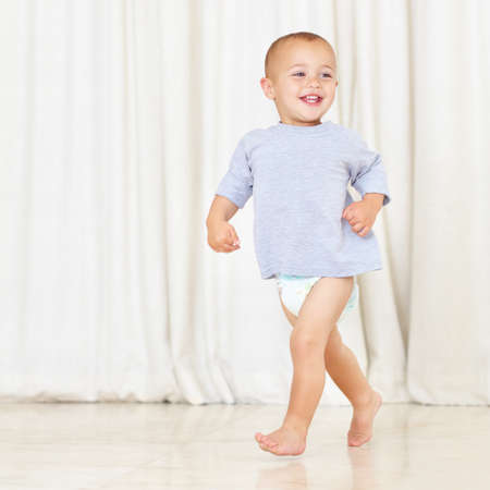 Strutting his stuff. Full length shot of a cute little boy walking around the house in a nappy and...