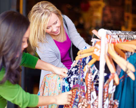 Raiding the sale rack. Two young woman looking through the sale items in a store together.の写真素材