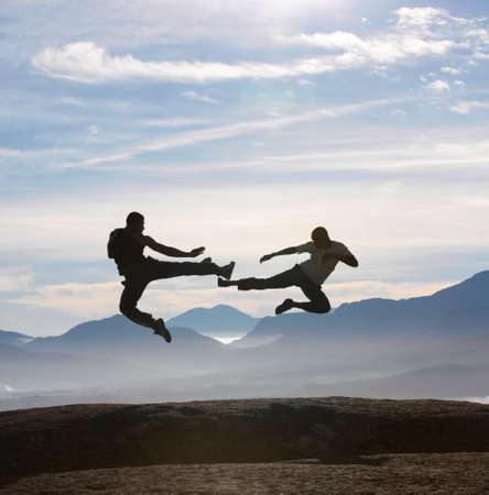 Flying feet on a mountain. Two male kickboxers fly kicking one another on a mountain top.