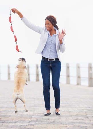 Jump higher. A beautiful african woman playing with her dog on the promenade.の写真素材