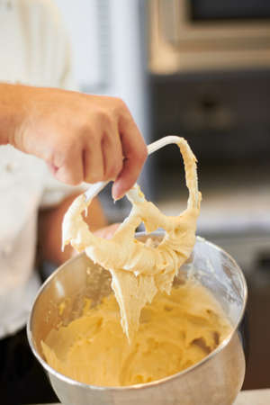 Mixing it until its smooth. A bowl of cupcake batter with the Baker holding up the mixer.