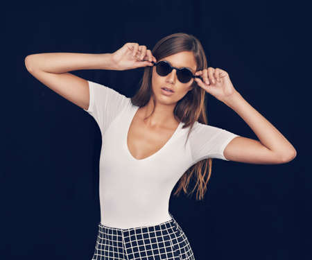 Keeping it cool. Studio shot of an attractive young woman holding her sunglasses.の写真素材