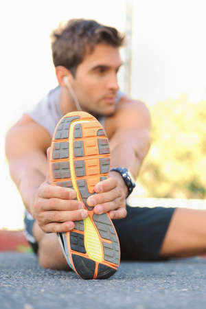 Stretching those muscles before a jog. Young jogger sitting and stretching while looking sideways.