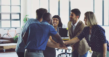 Lets go, team. Cropped shot of a group of young designers standing in the office with their hands in a huddle.の写真素材